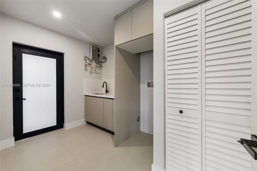 Utility space featuring custom cabinetry, integrated sink with matte black fixture, louvered closet doors, and black-framed glass-panel door
