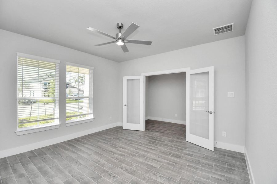 Experience the perfect blend of sophistication and warmth in this home office, boasting elegant wood-look tile flooring and flooded with natural light from expansive windows and French doors.