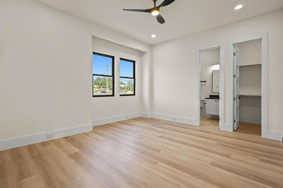 Unfurnished bedroom with connected bathroom, a spacious closet, ceiling fan, and light wood-type flooring