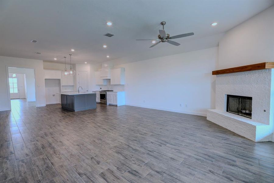 Unfurnished living room with baseboards, a fireplace with raised hearth, ceiling fan, wood finished floors, and recessed lighting