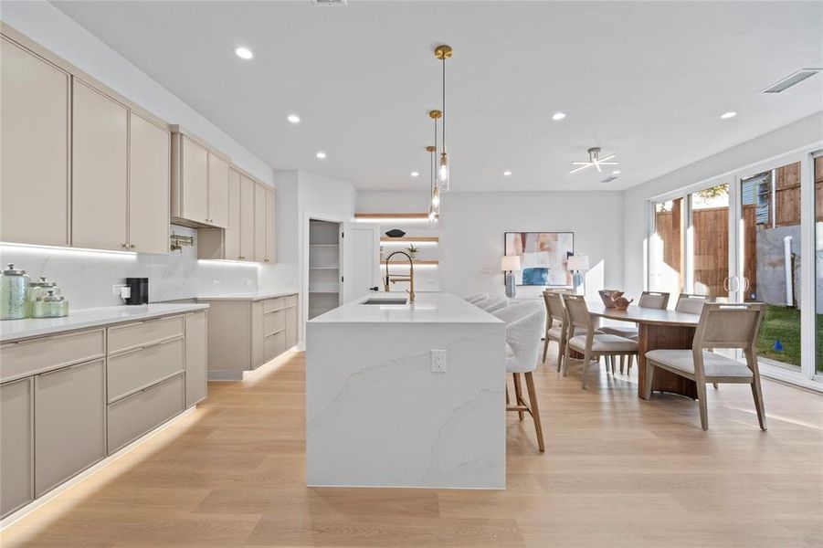 Kitchen featuring an island with sink, backsplash, sink, decorative light fixtures, and light wood-type flooring