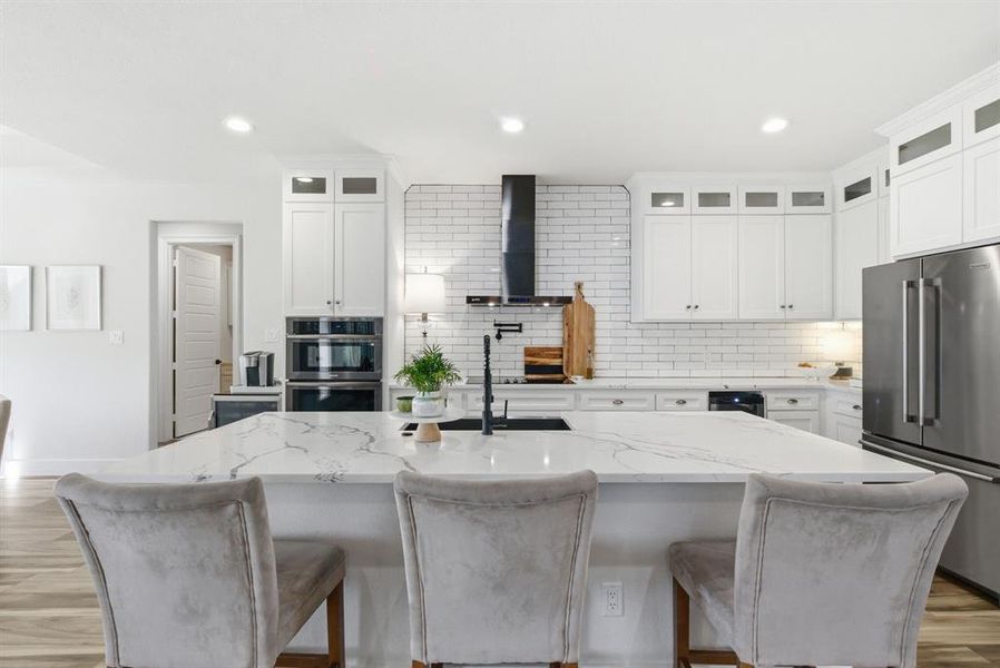 Kitchen featuring decorative backsplash, light wood-style floors, stainless steel appliances, white cabinets, and light stone counters
