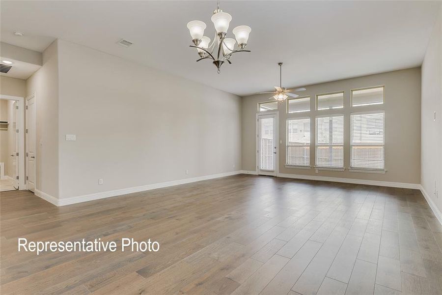 Spacious room featuring wood-finish flooring, a contemporary chandelier, a ceiling fan, multiple windows with blinds, and a white trim baseboard