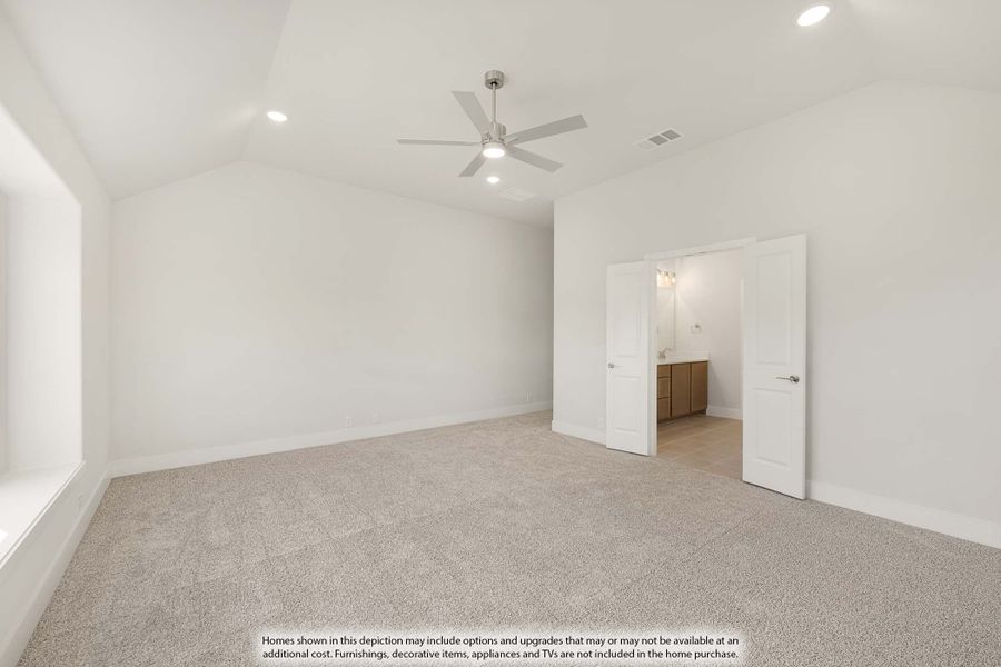 Empty master bedroom with vaulted ceiling, ceiling fan, carpet flooring, and ensuite bathroom doorway visible. Empty master bedroom with vaulted ceiling, ceiling fan, carpet flooring, and ensuite bathroom doorway visible.