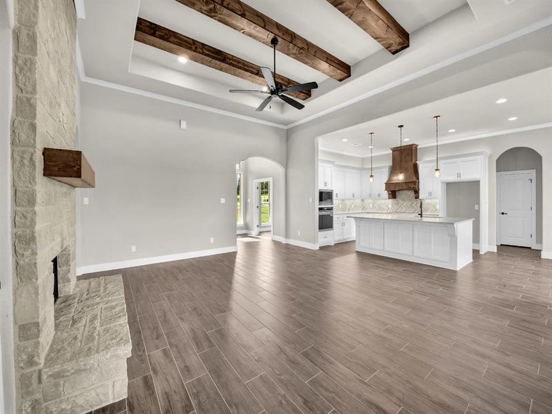Unfurnished living room with arched walkways, a stone fireplace, beam ceiling, wood finish floors, and recessed lighting Unfurnished living room with arched walkways, a stone fireplace, beam ceiling, wood finish floors, and recessed lighting