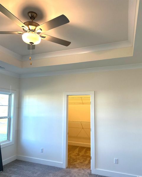 Empty room with dark carpet, ceiling fan, and crown molding