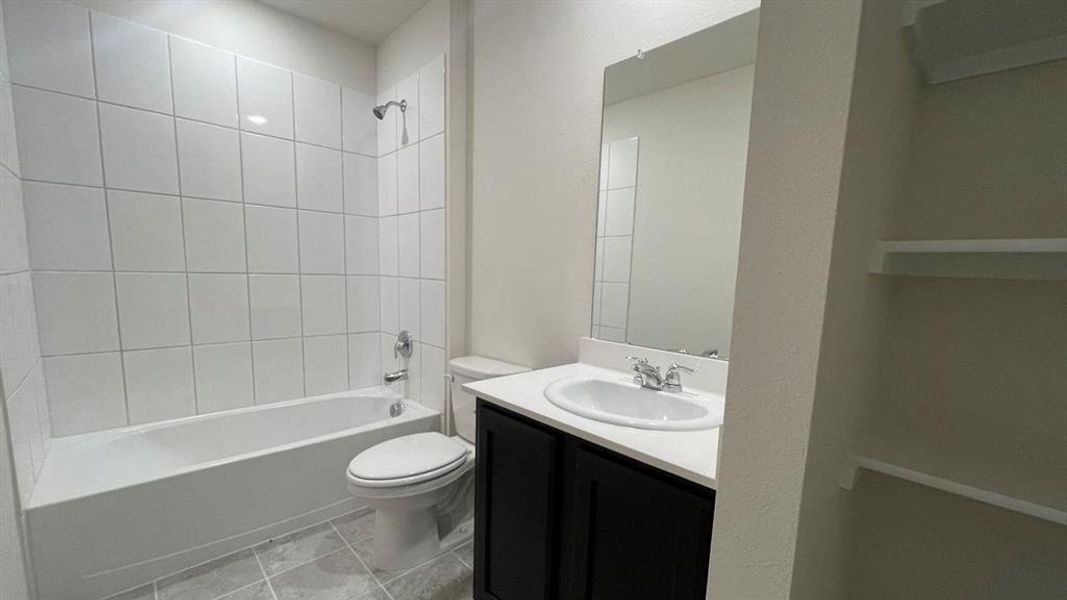 Contemporary bathroom featuring a tub-shower combination with white subway tile surround, a dark wood-finish vanity with an integrated sink and light-colored countertop, a large wall-mounted mirror, and tile flooring