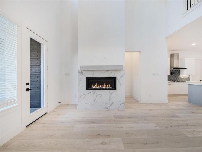 Unfurnished living room featuring a fireplace, light wood-style flooring, and a towering ceiling