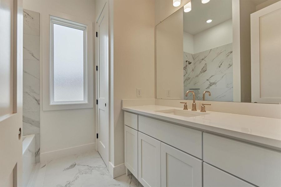 Elegant guest bath featuring quartz countertops, soft gold fixtures, and a beautifully tiled tub-shower—designed with both style and comfort in mind.