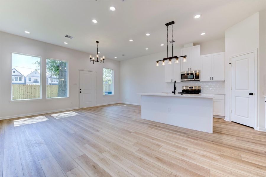 Open-concept living filled with natural light, featuring wood-look LVP flooring, tall ceilings, and a seamless flow between living, dining, and kitchen. Recessed lighting and statement fixtures add warmth, creating a bright and inviting everyday space.