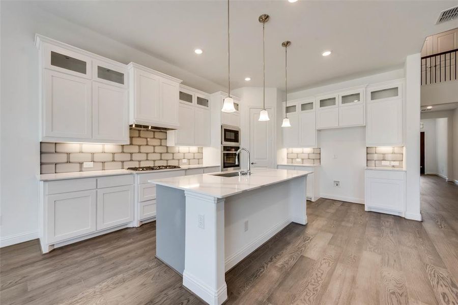 Kitchen featuring appliances with stainless steel finishes, wood-type flooring, a center island with sink, and decorative backsplash