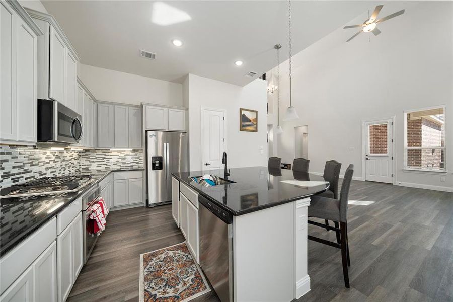 Kitchen featuring decorative light fixtures, stainless steel appliances, a kitchen breakfast bar, an island with sink, and dark hardwood / wood-style floors