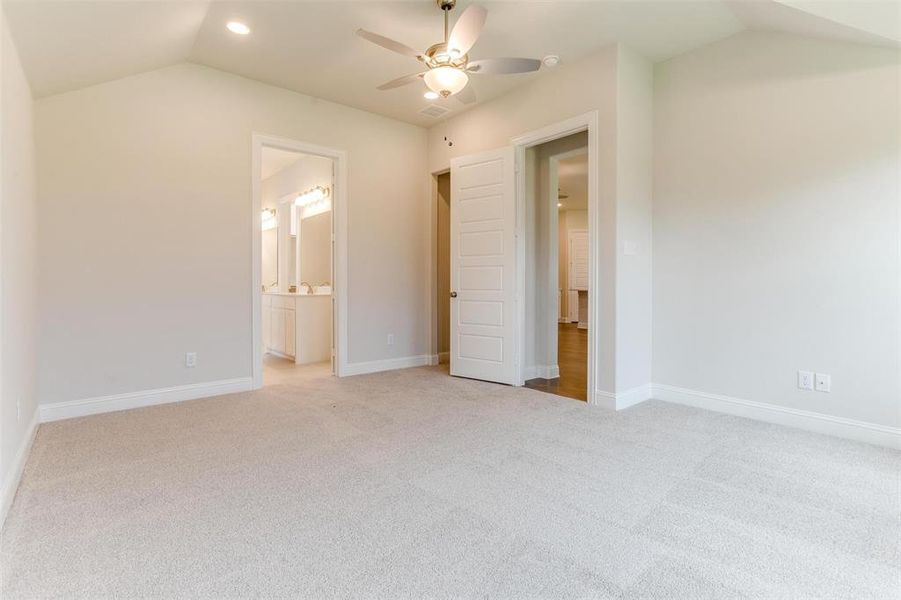 Unfurnished bedroom with light carpet, ceiling fan, connected bathroom, and vaulted ceiling