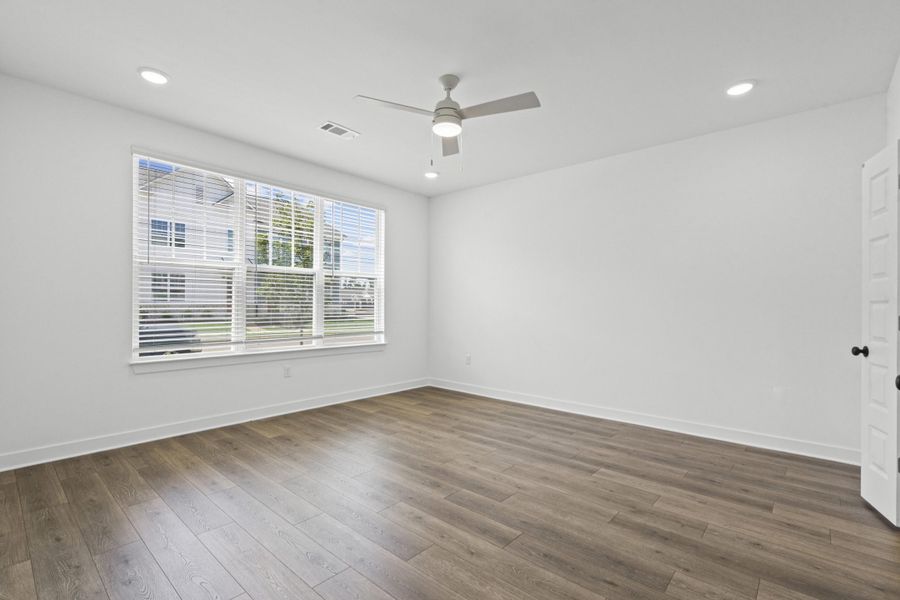 Spacious room featuring wood-finish flooring, a large multi-pane window with blinds, and white trim