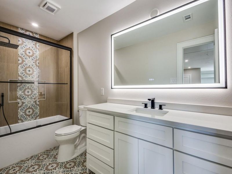 Upstairs bathroom with built in cabinets, lighted mirror with dimmer and anti-fog button, shower combo with glass door, and custom tiles-surrouund and patterned tile floors