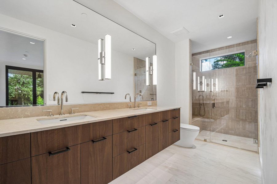 A sleek double vanity with stone countertops anchors this modern bathroom featuring a walk-in tile shower. A sleek double vanity with stone countertops anchors this modern bathroom featuring a walk-in tile shower.