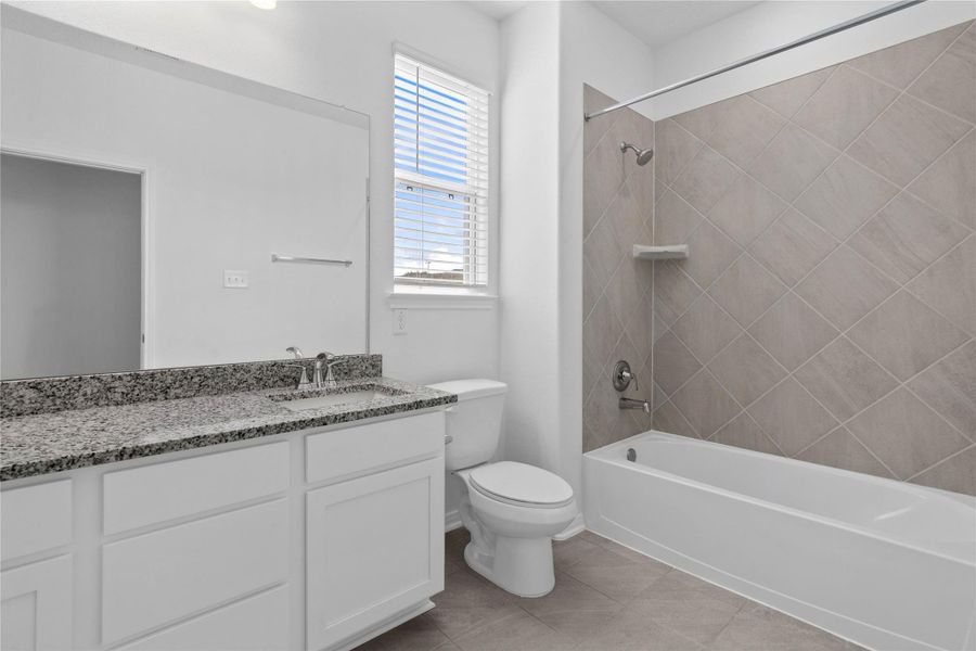 Well-appointed secondary bath with tub/shower combination and tile surround. It also features an extended vanity with granite countertop, a mirror that extends the full length of the vanity, and a window with privacy blinds.