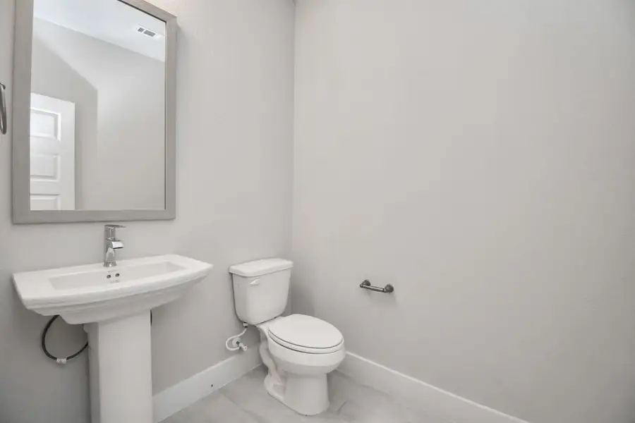 This half bathroom features a stylish pedestal sink, modern hardware, and bright recessed lighting, creating a sleek and inviting space. Sample photo of completed home with similar floor plan. Actual colors and selections may vary.