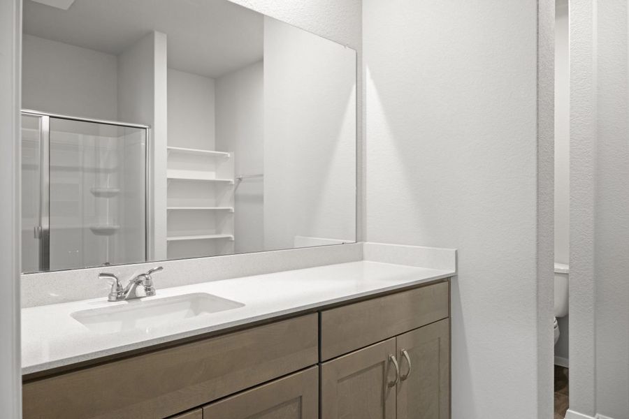 A bathroom with a white countertop, mirror, and brown cabinets, and white painted walls.