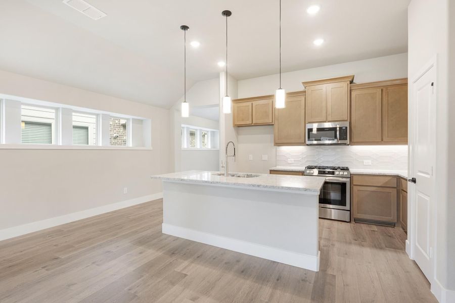 Kitchen with center island, granite countertops, wood cabinets, and stainless steel appliances on light hardwood floors
