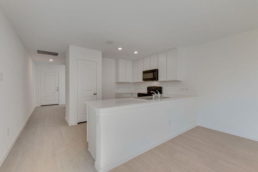 Kitchen featuring white cabinetry, a peninsula, black appliances, light wood-style floors, and recessed lighting