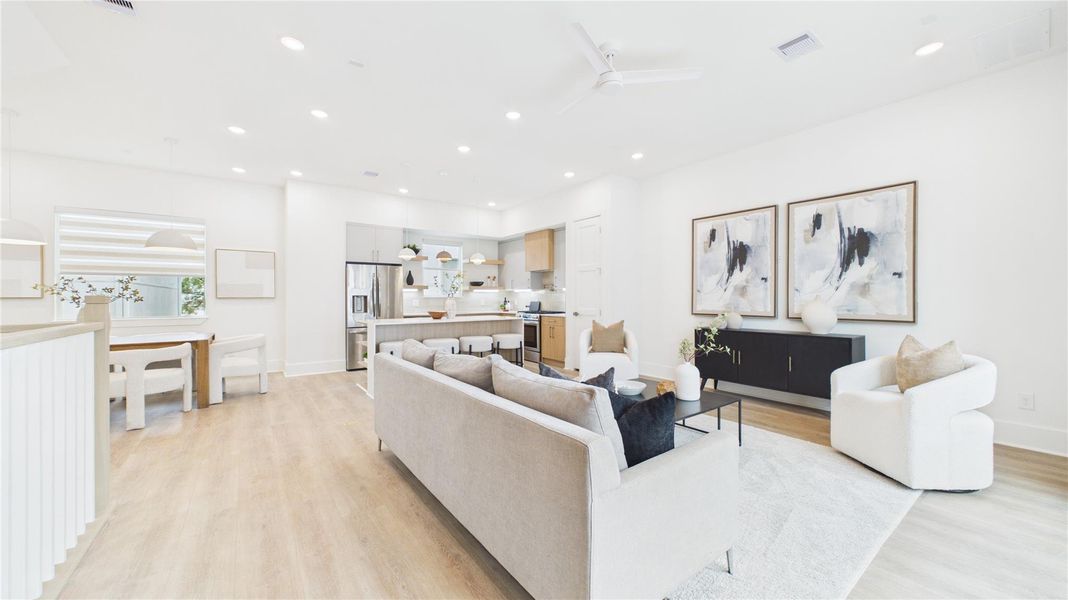 This photo showcases a bright, open-concept living space featuring a modern kitchen with stainless steel appliances and a cozy living area. The room has light wood flooring, contemporary furnishings, and elegant decor, creating a welcoming atmosphere.