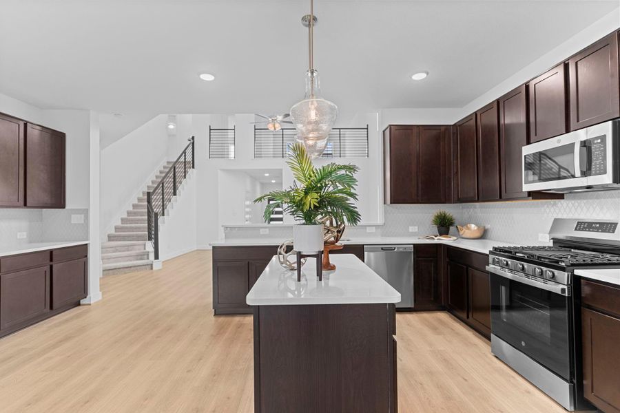 Expansive view of the kitchen and breakfast area featuring a large center island, modern pendant lighting, and open sightlines to the staircase and family room—designed for everyday comfort and entertaining. **Image Representative of Plan Only and May Vary as Built**.