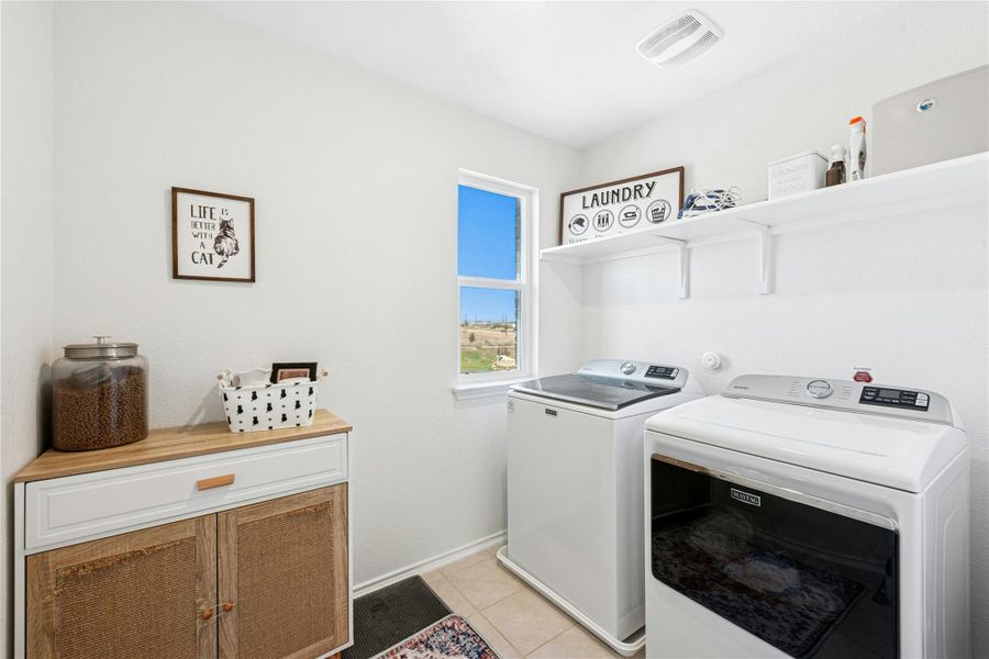 Laundry area with washer and dryer, light tile patterned floors, and cabinet space for storage and organization.
