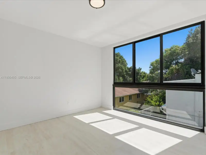 Expansive floor-to-ceiling windows with black frames, light-toned wood-finish flooring, and minimalist white walls Expansive floor-to-ceiling windows with black frames, light-toned wood-finish flooring, and minimalist white walls