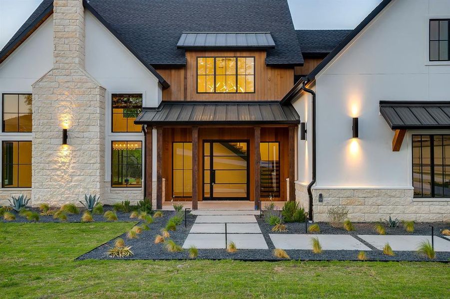 Doorway to property with stone siding, a standing seam roof, a shingled roof, and a lawn
