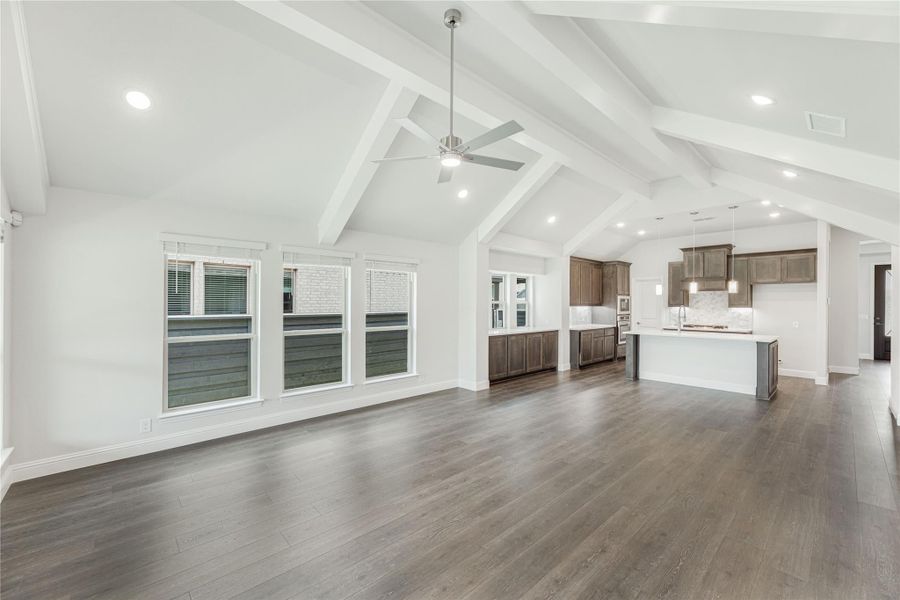 Open living area with vaulted beam ceiling, ceiling fan, dark hardwood floors, and open kitchen with wood cabinets in background Open living area with vaulted beam ceiling, ceiling fan, dark hardwood floors, and open kitchen with wood cabinets in background