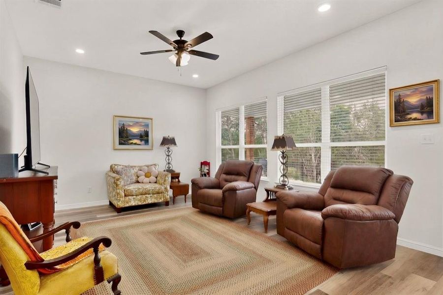 Spacious living area featuring light wood-finish flooring, a contemporary ceiling fan, and recessed lighting