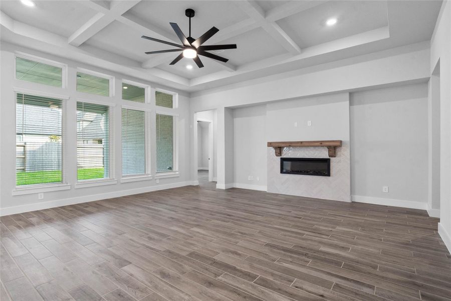 This expansive family room is a masterclass in modern design, featuring an electric fireplace with tile surround, soaring coffered ceilings, and a dramatic multi-blade designer fan. Massive floor-to-ceiling windows flood the space with natural light while offering serene views of the backyard. With its neutral palette and sleek tile flooring, this airy retreat is the perfect canvas for both grand entertaining and cozy movie nights.