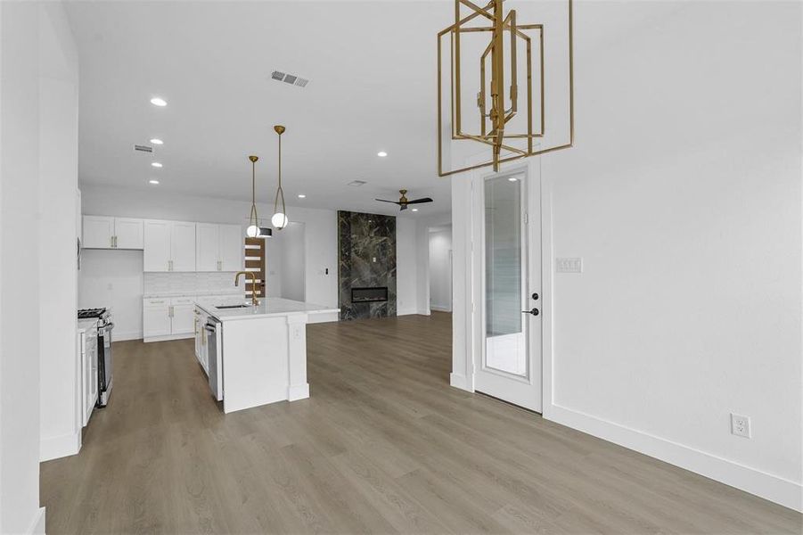 Kitchen with open floor plan, a fireplace, white cabinets, light countertops, and light wood-style flooring Kitchen with open floor plan, a fireplace, white cabinets, light countertops, and light wood-style flooring