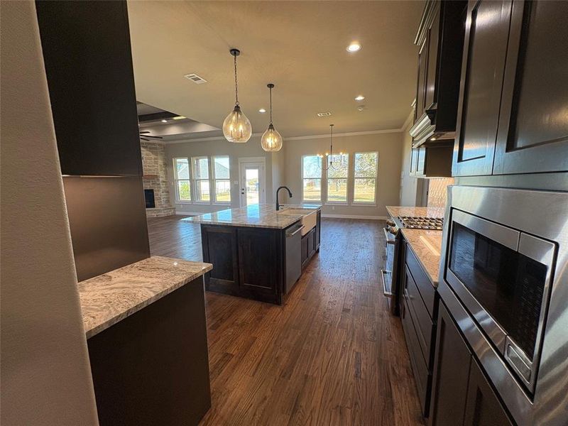 Kitchen with a stone fireplace, open floor plan, pendant lighting, recessed lighting, and an island with sink