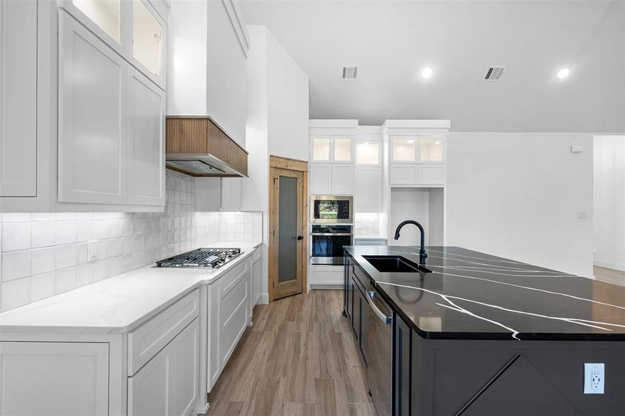 Kitchen featuring sink, light hardwood / wood-style floors, white cabinetry, and a center island with sink