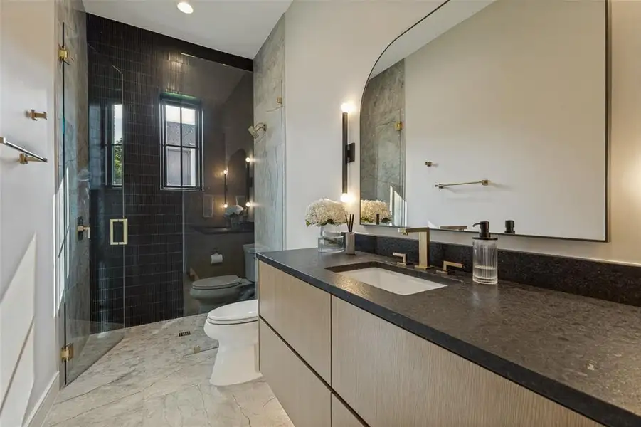 Bathroom featuring a wood-finish vanity with a dark countertop and integrated sink Bathroom featuring a wood-finish vanity with a dark countertop and integrated sink