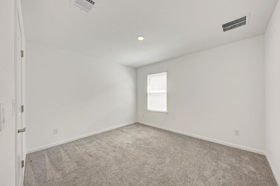 A well-lit bedroom offering a blank canvas for personalization, complete with soft carpeting and a window for natural illumination.