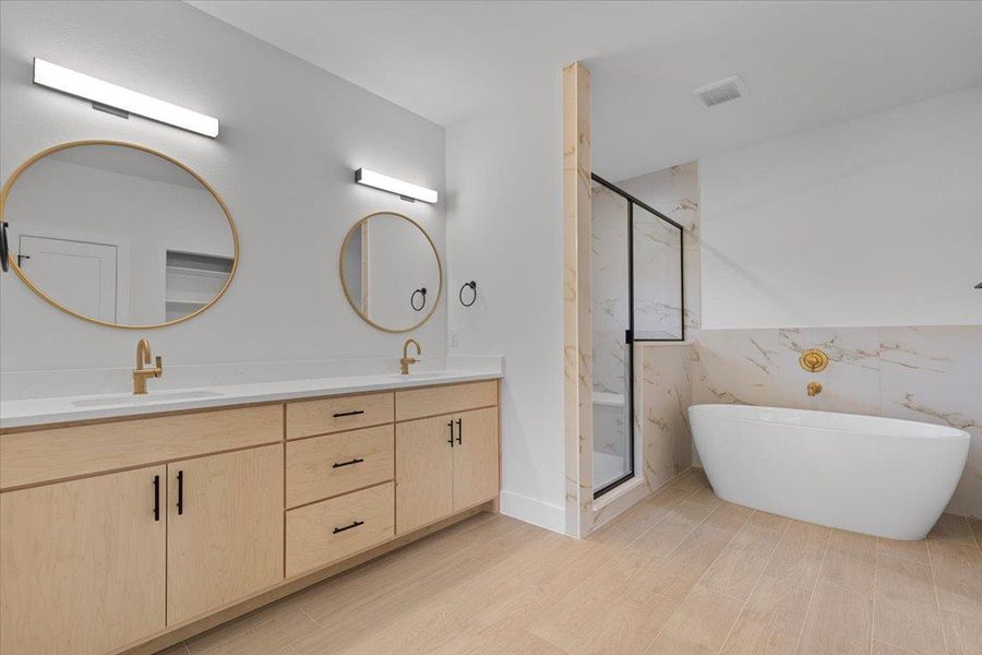 Bathroom featuring a marble finish shower, a freestanding tub, double vanity, light wood-type flooring, and tile walls Bathroom featuring a marble finish shower, a freestanding tub, double vanity, light wood-type flooring, and tile walls