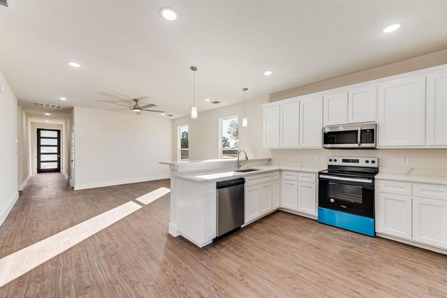 Kitchen featuring stainless steel appliances, white cabinetry, decorative light fixtures, light hardwood / wood-style floors, and kitchen peninsula