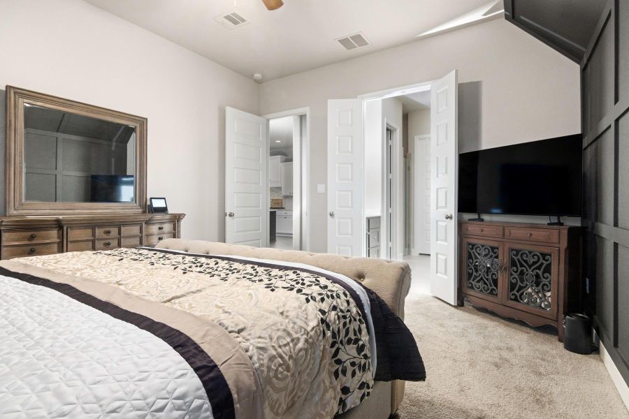 This bedroom features a cozy and elegant design with plush carpeting, Double doors lead to an adjoining bathroom, enhancing the spacious feel.