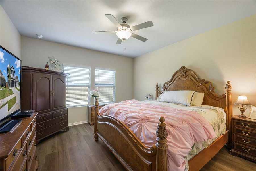 Bedroom featuring wood-finish flooring, two windows with blinds, and a ceiling fan with integrated lighting Bedroom featuring wood-finish flooring, two windows with blinds, and a ceiling fan with integrated lighting