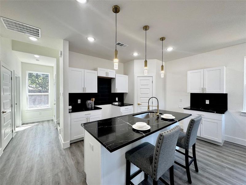 Kitchen with a center island with sink, white cabinetry, sink, and tasteful backsplash