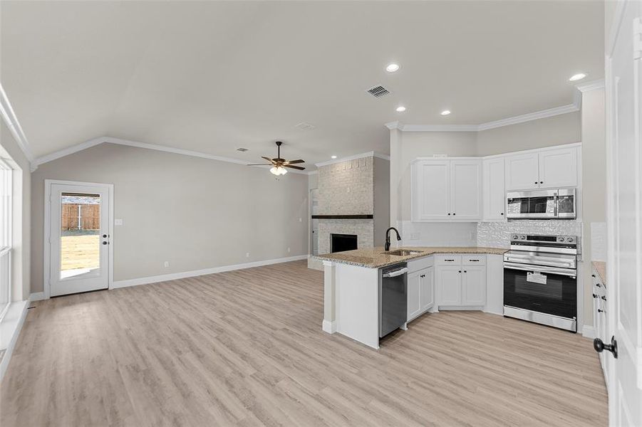 Kitchen featuring a peninsula, open floor plan, stainless steel appliances, a fireplace, and white cabinets