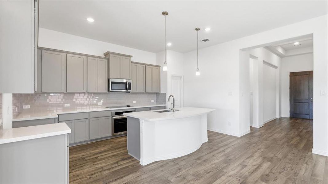 Open-concept kitchen featuring an arc-shaped island with an undermount sink, pendant lighting, shaker-style cabinetry, a subway tile backsplash, and wood-finish flooring