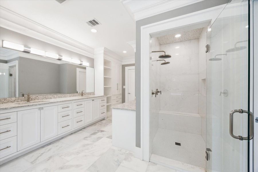 Another view of the primary bathroom featuring the spacious design with dual sinks, a large vanity with ample storage, a modern over-sized glass-enclosed shower, and elegant marble flooring.