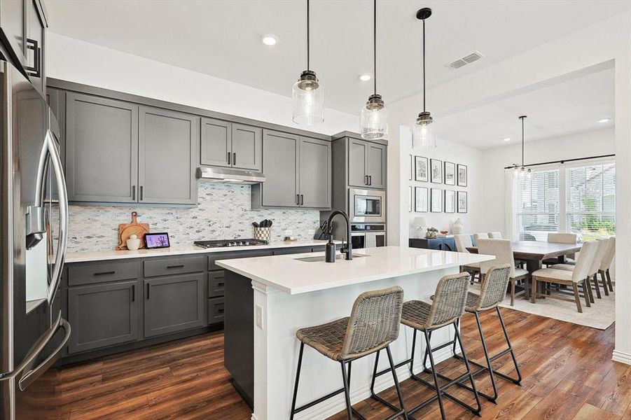 Kitchen with gray cabinets, decorative light fixtures, dark hardwood / wood-style flooring, appliances with stainless steel finishes, and backsplash