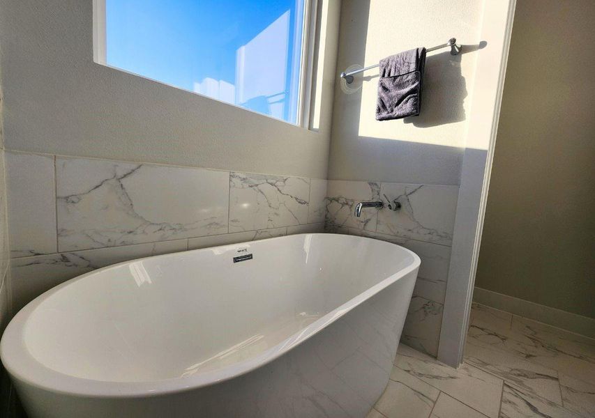 This photo showcases a modern bathroom with a freestanding white bathtub, accented by elegant marble-patterned tiles. Natural light streams in through a window, enhancing the clean and serene atmosphere. This photo showcases a modern bathroom with a freestanding white bathtub, accented by elegant marble-patterned tiles. Natural light streams in through a window, enhancing the clean and serene atmosphere.