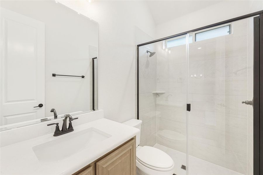 Bathroom with wood vanity, white countertop, and glass-enclosed tile shower with black fixtures Bathroom with wood vanity, white countertop, and glass-enclosed tile shower with black fixtures