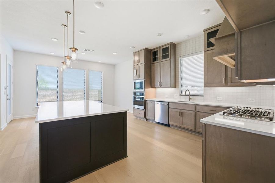 Contemporary kitchen featuring a large central island with a white countertop, light wood-finish flooring, recessed lighting, and a suite of stainless steel appliances Contemporary kitchen featuring a large central island with a white countertop, light wood-finish flooring, recessed lighting, and a suite of stainless steel appliances